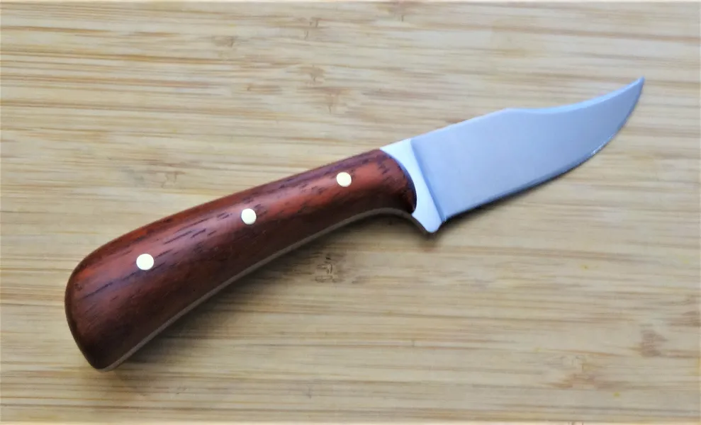 Full Right side of Paduak upswept clip point neck knife showcasing brass pins, on wooden surface