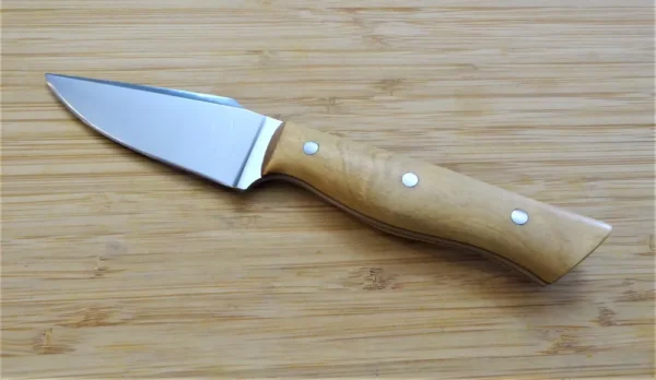 Left side of Palatka Holly Harpoon Clip Point #211 Knife showcasing 1095 high carbon steel blade and mild steel pins on wooden surface