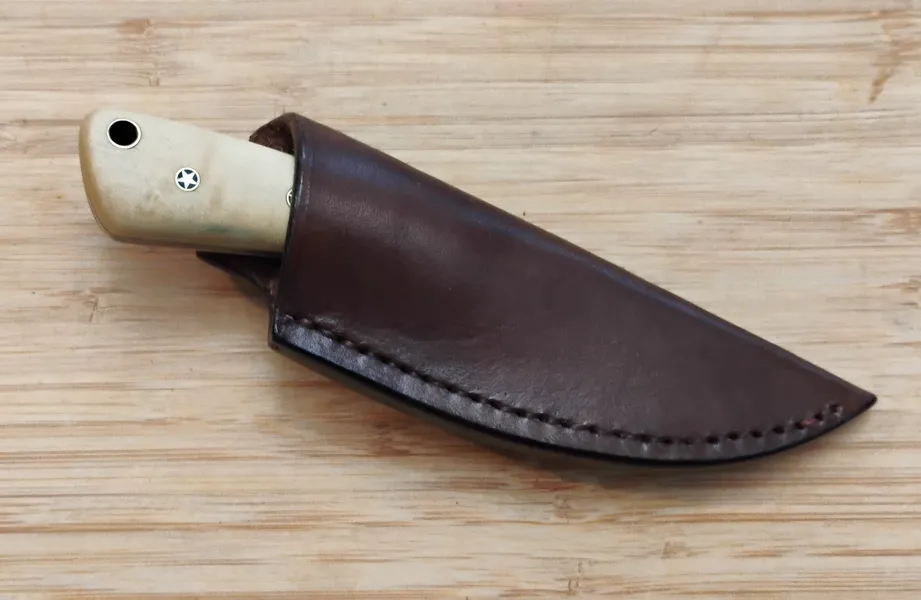 Southern Magnolia Caping Knife #327 in a custom leather pouch sheath, displayed on a bamboo cutting board.