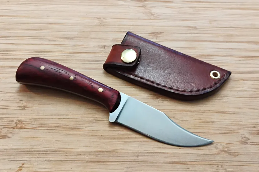 Upswept Clip Point with Padauk handle next to custom leather sheath