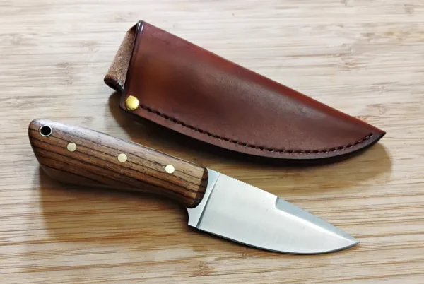 Zebrawood 3 Finger Skinner #303 sitting next to leather Pouch sheath on a wooden background