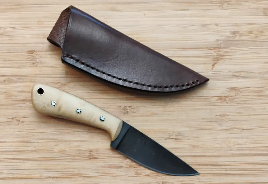 Southern Magnolia Caping Knife #327 next to a custom leather pouch sheath, displayed on a bamboo cutting board.