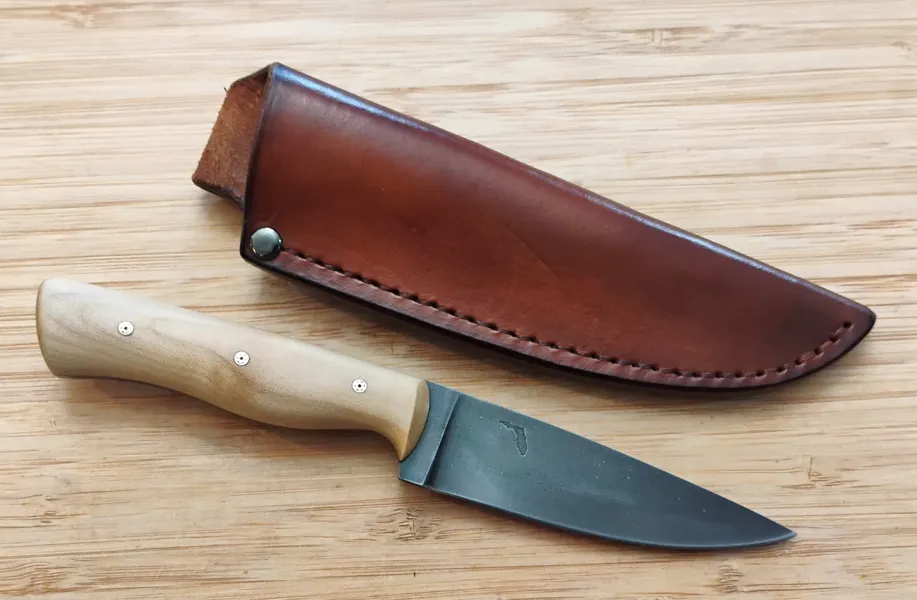 Southern Magnolia Bird Trout Knife beside custom leather sheath