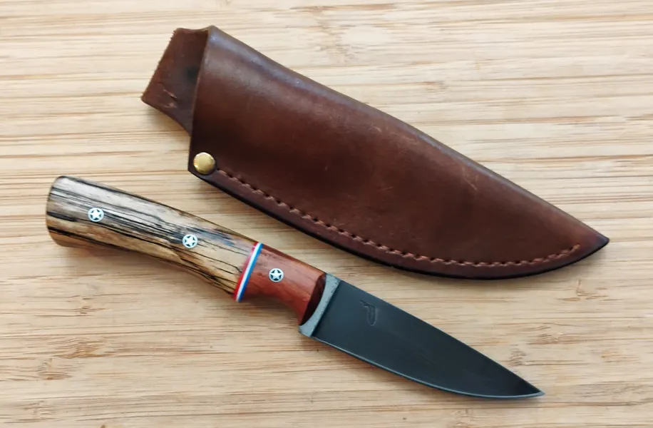 Spalted Pecan Bird & Trout hunting knife next to custom leather pouch sheath on wooden surface.