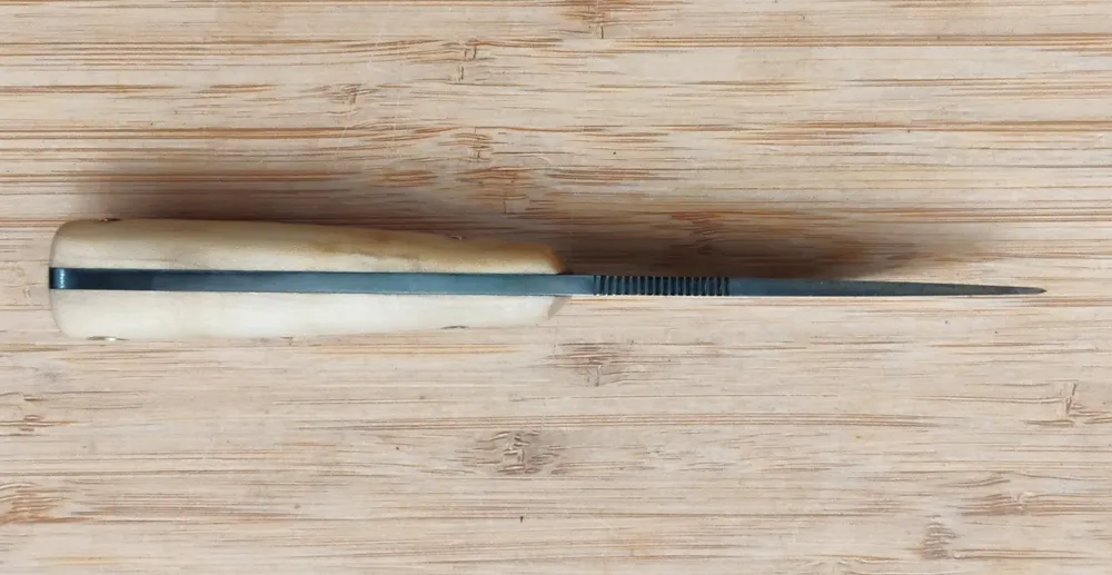 Southern Magnolia Caping Knife #327 high carbon steel spine view highlighting thumb serrations on a bamboo cutting board.