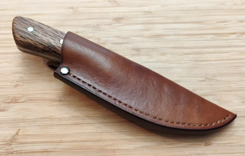 Drop Point EDC/Hunter knife with a Southern Red Oak handle inserted into its brown leather sheath.