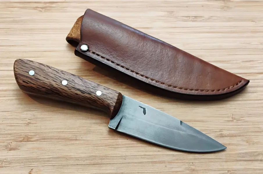 EDC/Hunter knife with an Antiqued finish placed next to its brown leather sheath, featuring a Florida Southern Red Oak handle