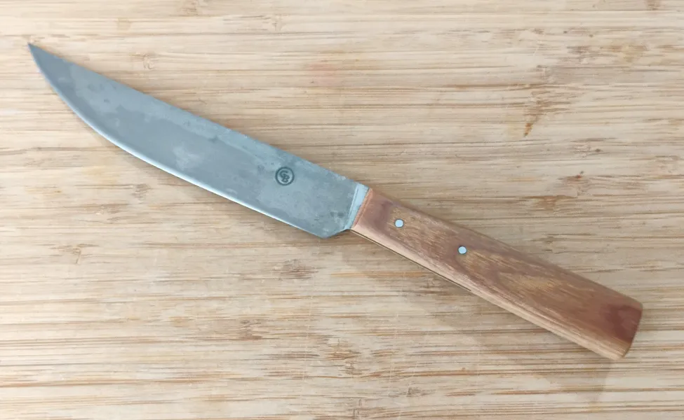 Left side view of Hard Maple Trade Knife #356 on wooden surface, showcasing antiqued 1095 high carbon steel blade and stabilized hard maple handle."