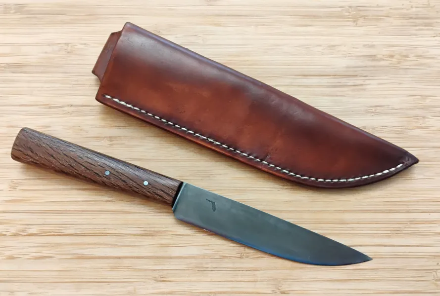 Live Oak French Trade Knife #361 next to its brown Oak Bark leather sheath with white linen stitches on a wooden surface