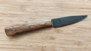 Bur Oak Tiny Trade Knife #363 right side view on wooden surface, showing antiqued 1095 high carbon steel blade with steel pins.