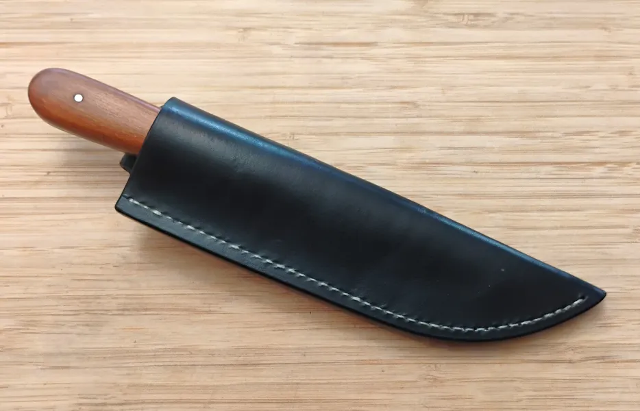 Pernambuco Trade Knife in a Vinegaroon Black sheath with white linen stitching finished with bees wax on a wooden background.