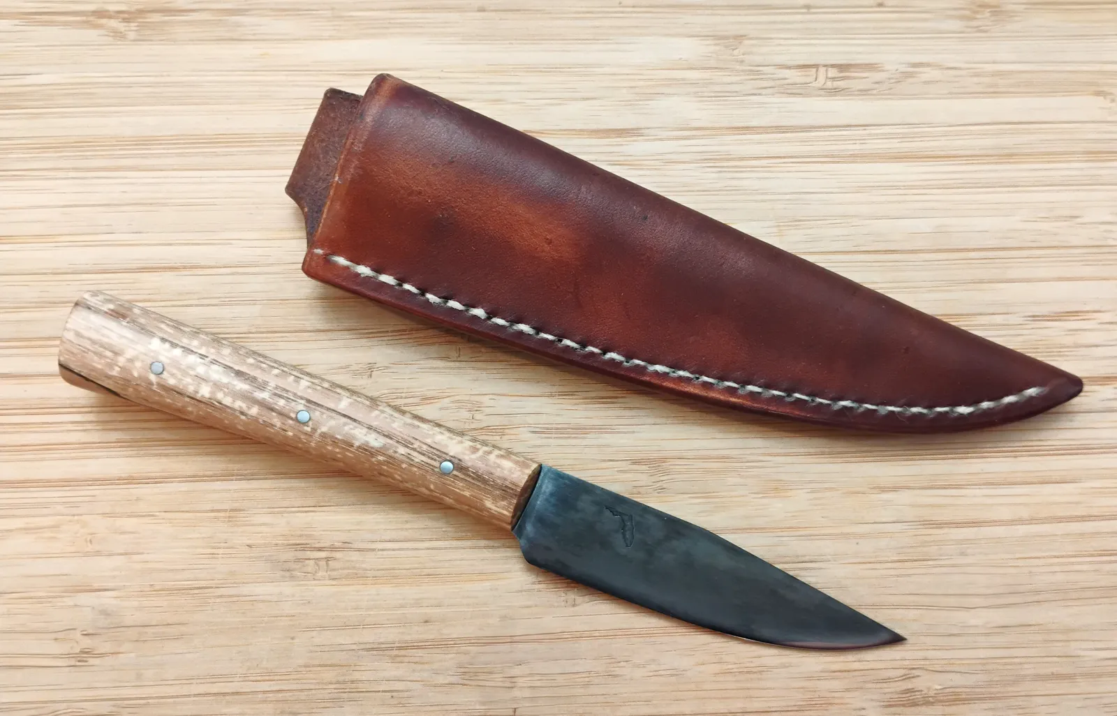 Pecan Trade Knife next to its custom Oak Bark-dyed leather sheath, showing the lightweight 7 1/4" design on a wood background.