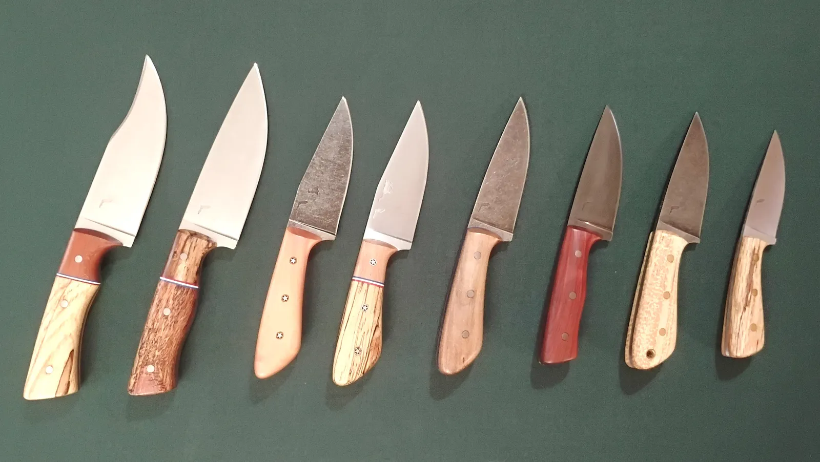 Eight custom knives with an assortment of Florida wood handles, arranged largest to smallest with different blade finishes.