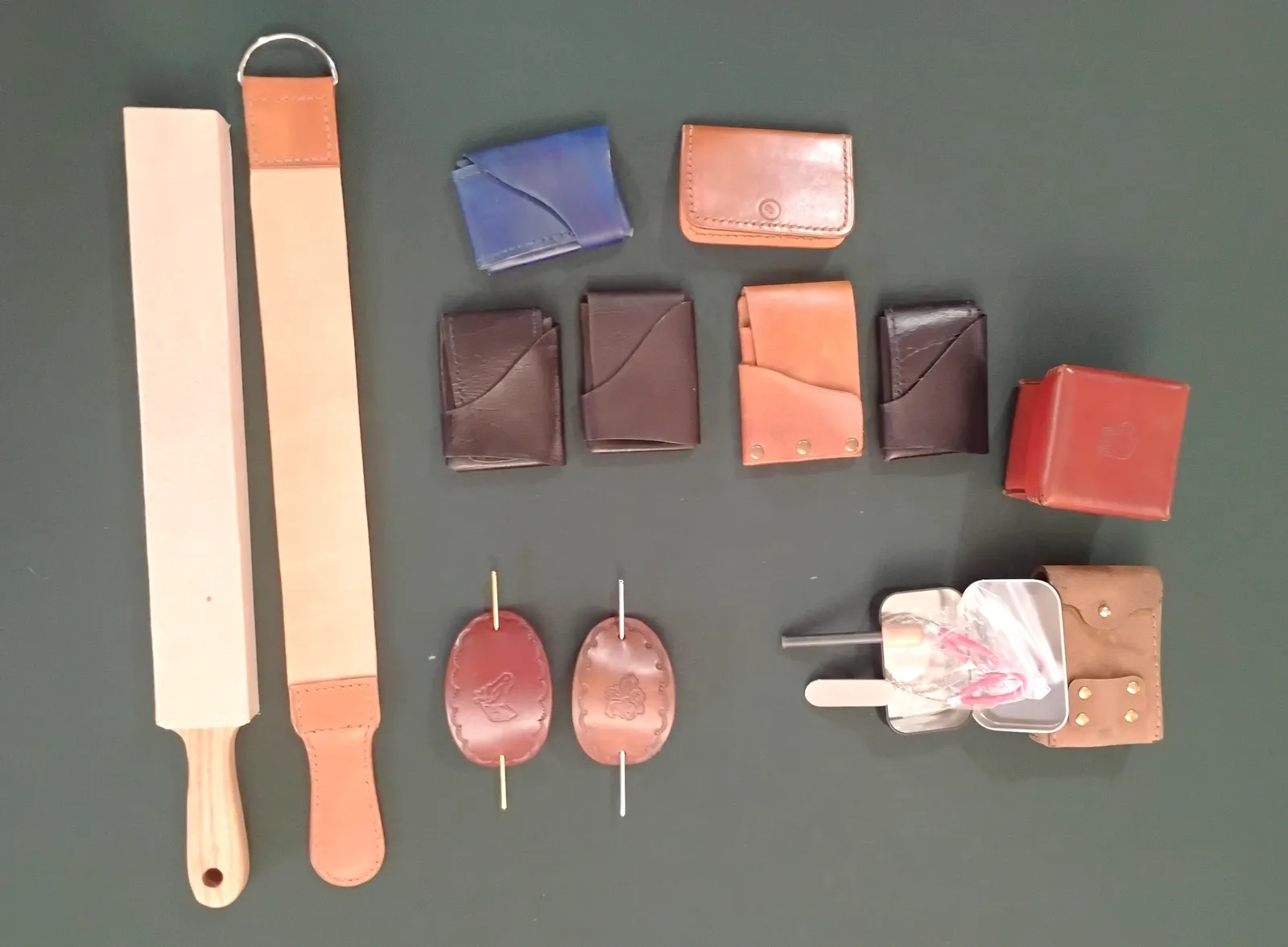 Leather goods - minimalist wallets, hair wraps, fire starter kits on a green backgroud, ready for market.