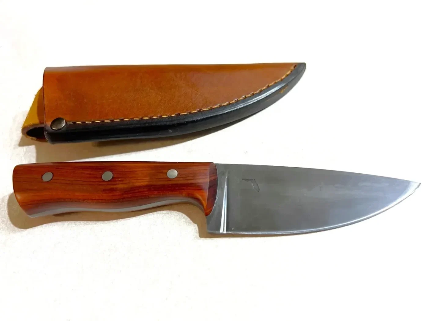 Little Camper custom knife by GreBec Knives sitting next to a veg-tanned custom leather sheath.