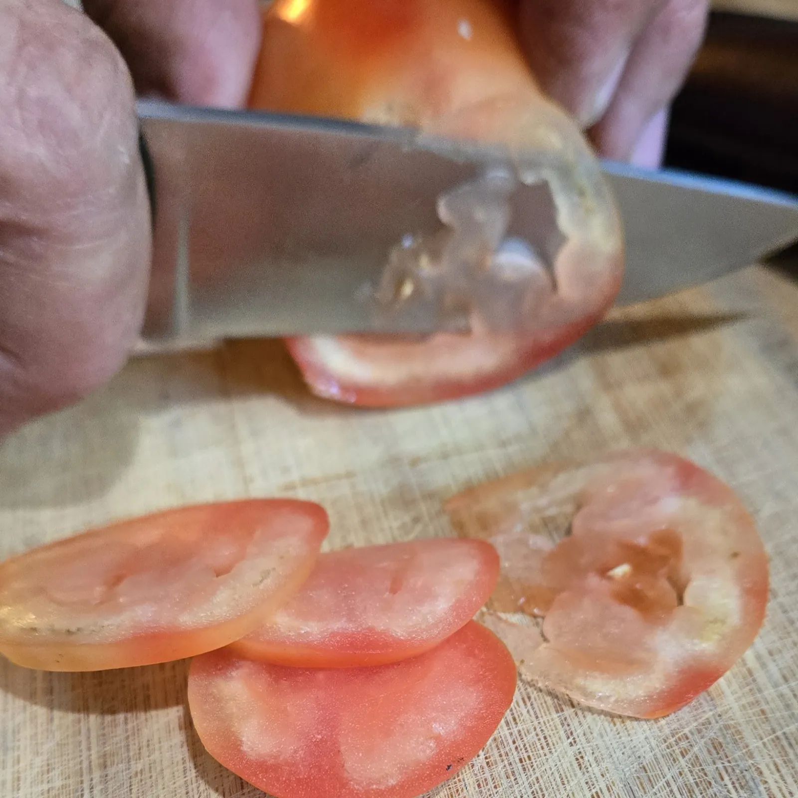The custom knife from GreBec Knives effortlessly slicing a tomato into ultra-thin, even slices on a cutting board.
