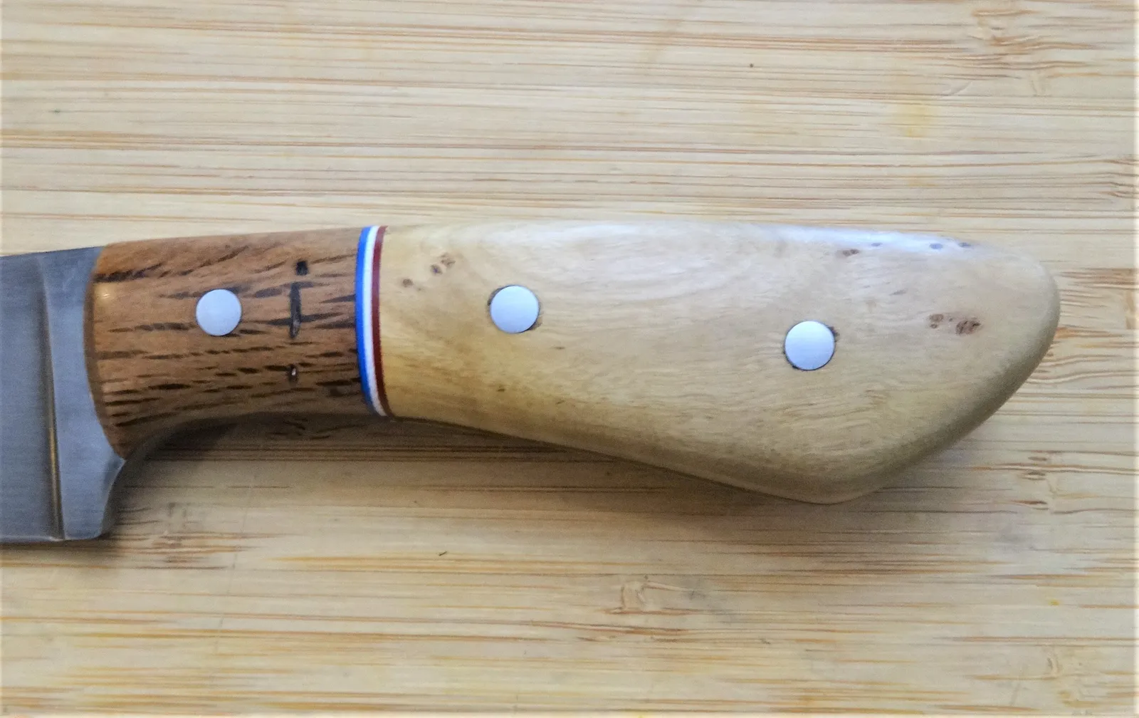 Left view of a crepe myrtle and live oak custom knife handle with red, white and blue spacers and mild steel pins.