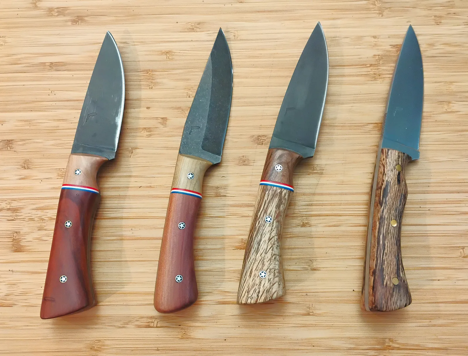 Four knives with drop point and clip point blades and different stabilized wood handles sitting next to each other.