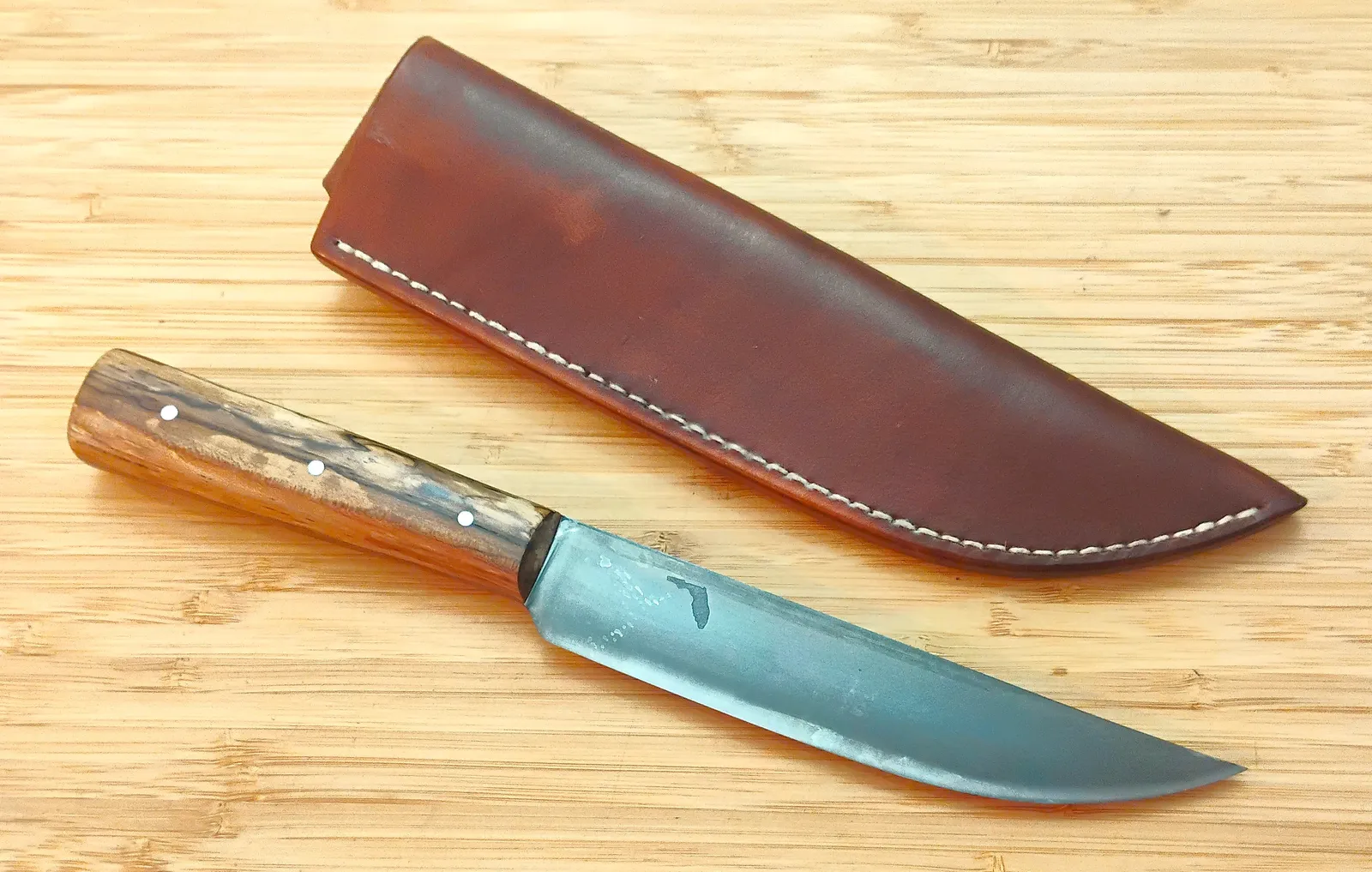 The Spalted Pacan Trade Knife sitting next to a brown, oak bark hand dyed sheath and stitched with white linen thread.