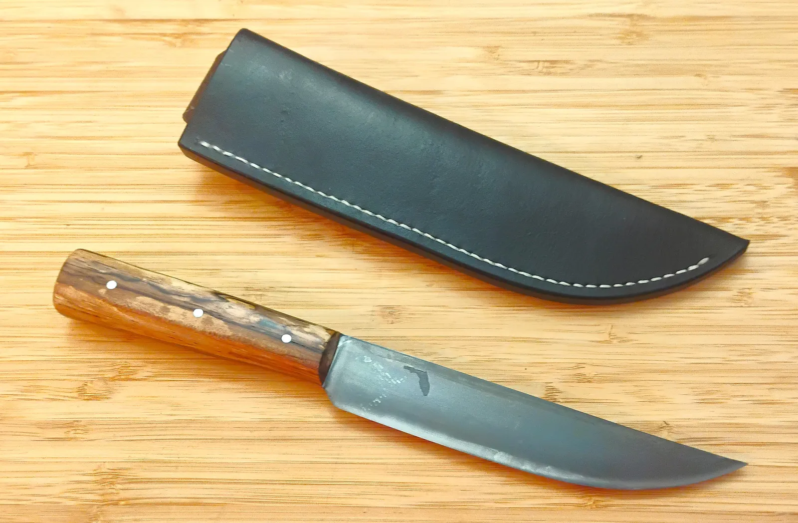 The Spalted Pacan Trade Knife sitting next to a custom black, vinegaroon, hand dyed sheath and stitched with white linen thread.
